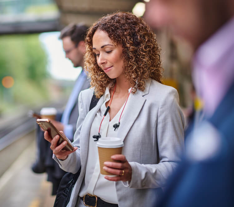 Woman in smart clothing looking at smart phone and holding coffee cup
