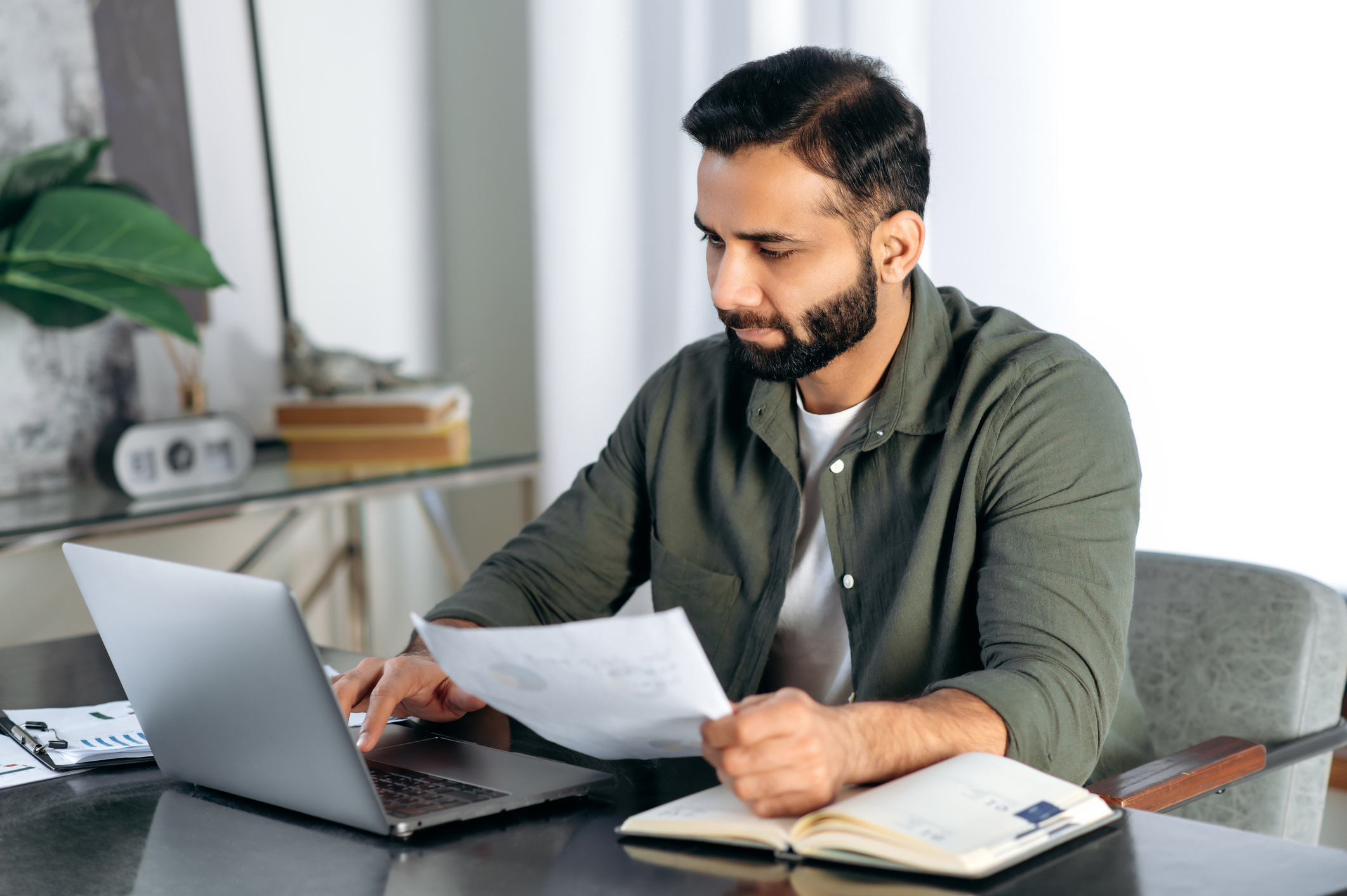 Man working at laptop holding documents