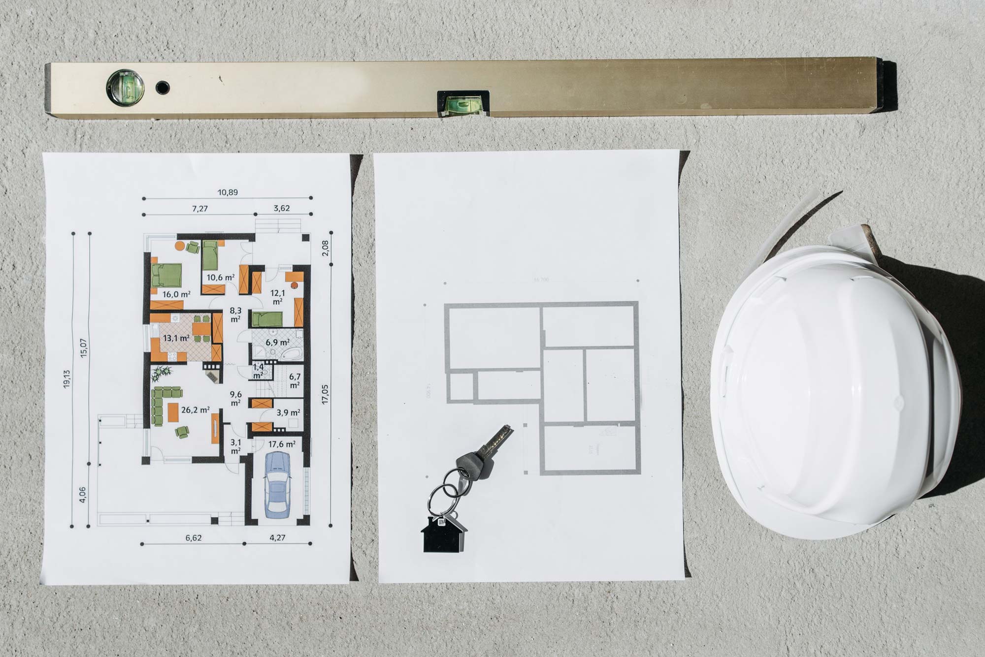 A flatlay image of building plans, a hard hat and a spirit level.